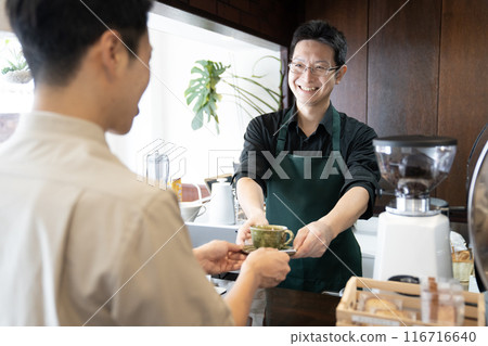 A male cafe attendant handing coffee to a customer A male cafe attendant handing coffee to a customer 116716640