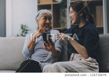 Cheerful mother and pretty teenager kid relaxing at cozy home, using mobile phone for Internet communication, resting on sofa with digital gadget, enjoying leisure, looking at camera Cheerful mother and pretty teenager kid relaxing at cozy home, using mobile phone for Internet communication, resting on sofa with digital gadget, enjoying leisure, looking at camera 116716676