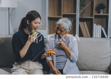 Happy asian woman daughter hugging senior mother in the kitchen room eating healthy food happy enjoying. Happy asian woman daughter hugging senior mother in the kitchen room eating healthy food happy enjoying. 116716690