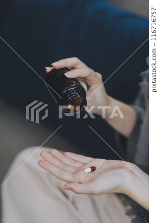 A woman with a cold with pills is treated at home chooses which drugs to take and self-medicates, checks the expiration date while sitting on the couch at home 116716757