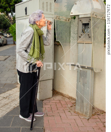 Time Stands Still: Senior Woman Inspects Abandoned Payphone, Reflects on the Pace of Progress 116717672