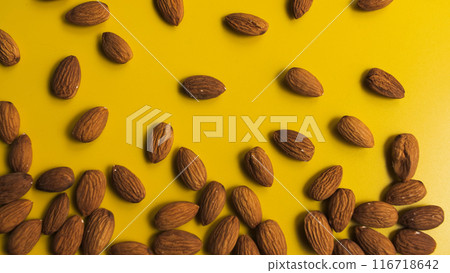 Vibrant close-up of scattered almonds on a bright yellow background Vibrant close-up of scattered almonds on a bright yellow background 116718642
