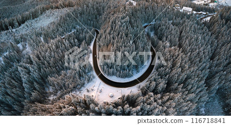 Aerial view of winter landscape with snow covered mountain hills and winding forest road in morning. 116718841
