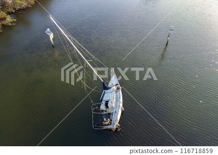 Aerial view of sunken sailboat on shallow bay waters after hurricane in Manasota, Florida Aerial view of sunken sailboat on shallow bay waters after hurricane in Manasota, Florida 116718859