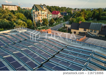 Aerial view of solar power plant with blue photovoltaic panels mounted on industrial building roof for producing green ecological electricity. Production of sustainable energy concept Aerial view of solar power plant with blue photovoltaic panels mounted on industrial building roof for producing green ecological electricity. Production of sustainable energy concept 116718866