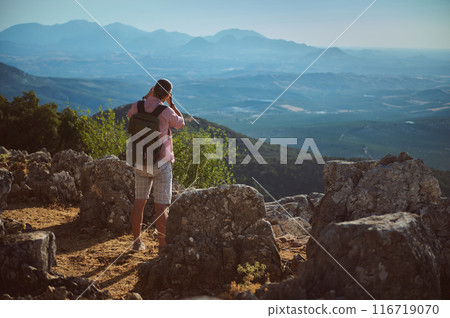 Hiker photographing mountain landscape with backpack on rocky terrain Hiker photographing mountain landscape with backpack on rocky terrain 116719070