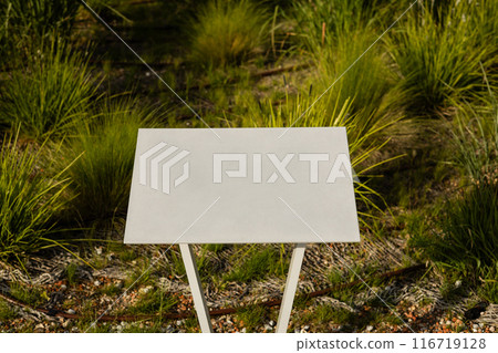 Closeup white metal sign at green grass background, nameplate with a space for your text. Horizontal banner 116719128
