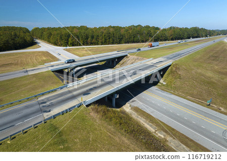 Aerial view of freeway overpass junction with fast moving traffic cars and trucks in american rural area. Interstate transportation infrastructure in USA Aerial view of freeway overpass junction with fast moving traffic cars and trucks in american rural area. Interstate transportation infrastructure in USA 116719212