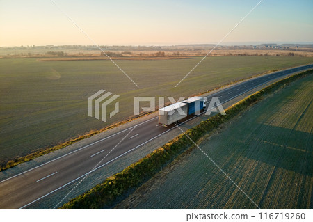 Aerial view of blurred fast moving semi-truck with cargo trailer driving on highway hauling goods in evening. Delivery transportation and logistics concept Aerial view of blurred fast moving semi-truck with cargo trailer driving on highway hauling goods in evening. Delivery transportation and logistics concept 116719260