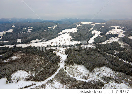 Aerial view of barren winter landscape with mountain hills covered with evergreen pine forest after heavy snowfall on cold quiet evening. Aerial view of barren winter landscape with mountain hills covered with evergreen pine forest after heavy snowfall on cold quiet evening. 116719287