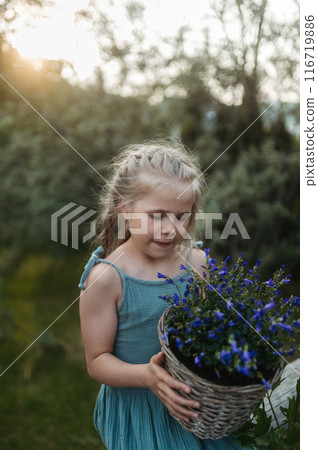 Potrait of little girl taking care of flowers in the garden, holding purple flower bells in pot. 116719886