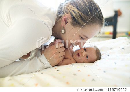 Mom kissing cheek of newborn baby, looking at infant lovingly. Unconditional paternal love, Mother's Day concept. Mom kissing cheek of newborn baby, looking at infant lovingly. Unconditional paternal love, Mother's Day concept. 116719922