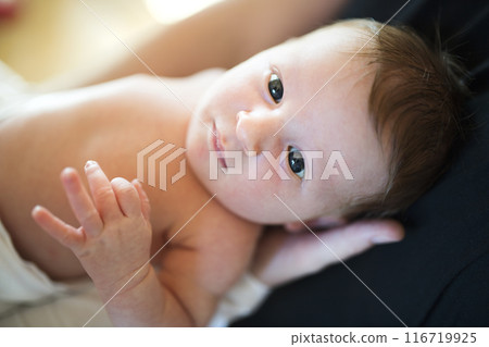 Portrait of cute little baby lying on bed, parents hands holding her. Portrait of cute little baby lying on bed, parents hands holding her. 116719925