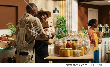 African american supplier giving fresh produce in crates to merchant, working on restocking merchandise with freshly harvested goods. Farmer and vendor collaborating on supplying store. Camera 1. African american supplier giving fresh produce in crates to merchant, working on restocking merchandise with freshly harvested goods. Farmer and vendor collaborating on supplying store. Camera 1. 116720389