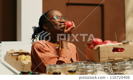African american buyer enjoying fresh aroma of tomatoes at store, smelling freshly harvested produce placed in crates at neighborhood supermarket. Woman supporting local farming. Camera 1. 116720406
