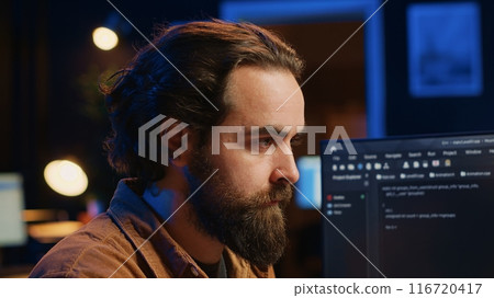 Focused software developer in home office doing coding on computer at desk, close up. IT specialist paying close attention to screen, writing lines of code at workstation, camera A 116720417