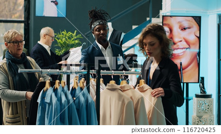 Employees team presenting variety of clothes to senior client, helping her to choose the perfect shirt size to create a formal outfit. Diverse store assistants show clothing from designers. Camera A. Employees team presenting variety of clothes to senior client, helping her to choose the perfect shirt size to create a formal outfit. Diverse store assistants show clothing from designers. Camera A. 116720425