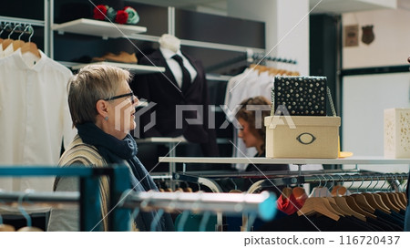 Elderly client asking to see multiple trendy bags in clothing store, talking to shop assistant about recommendations. African american worker shows different designer accessories. Camera A. Elderly client asking to see multiple trendy bags in clothing store, talking to shop assistant about recommendations. African american worker shows different designer accessories. Camera A. 116720437