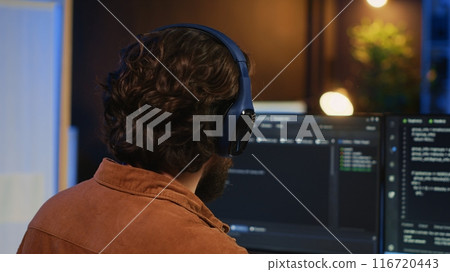 Man doing IT support job from apartment office, drinking cup of coffee and listening music while coding. Developer with headphones on enjoying hot tea and writing code on computer, camera A close up Man doing IT support job from apartment office, drinking cup of coffee and listening music while coding. Developer with headphones on enjoying hot tea and writing code on computer, camera A close up 116720443