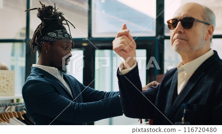 Famous couturier giving order to store assistant to help with finding a tie for his african american client, experienced senior tailor in. Fashion designer shopping for luxury accessories. Camera A. 116720480