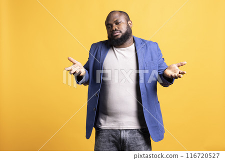 Uncaring african american man shrugging shoulders, showing indifference and apathy. Careless BIPOC person doing nonchalant indifferent hand gesturing, isolated over studio background Uncaring african american man shrugging shoulders, showing indifference and apathy. Careless BIPOC person doing nonchalant indifferent hand gesturing, isolated over studio background 116720527