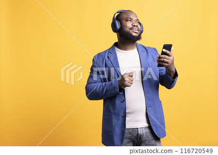 Relaxed african american man having fun listening to music from mobile phone. Carefree BIPOC person hearing tunes playing from smartphone device, isolated over studio background 116720549