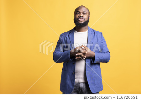Uneasy african american man posing and holding hands together, isolated over yellow studio background. BIPOC person feeling anxious, waiting for something, looking to the side Uneasy african american man posing and holding hands together, isolated over yellow studio background. BIPOC person feeling anxious, waiting for something, looking to the side 116720551