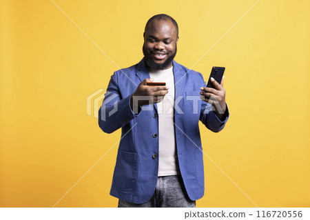 Upbeat man adding payment method on phone, enjoying himself, isolated over studio background. Joyous person delighted to do internet shopping, carefully typing credit card information 116720556