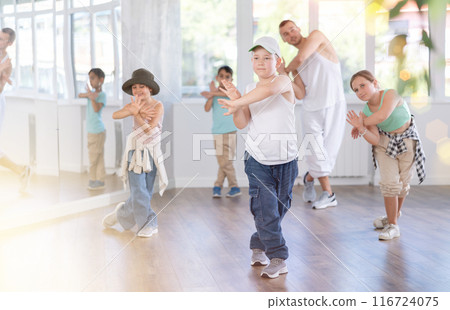 Young happy boy and group of positive children practicing energetic hip hop movements at dance school Young happy boy and group of positive children practicing energetic hip hop movements at dance school 116724075