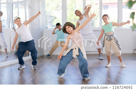 Happy enthusiastic teen girl honing hip-hop moves in dance studio setting with group of children 116724091