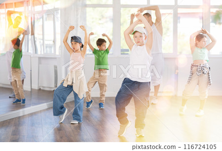 In sports studio, childrens team learns hip-hop dance accompanied by experienced man teacher 116724105