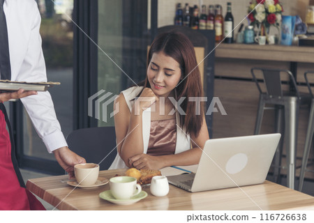 Restaurant business Handsome waiter serving food to young beautiful women with smiling face. Businesswoman using computer laptop while working on luch time. Waiter Man serving coffee cup in cafe 116726638