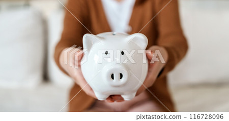 Woman hand holding piggy bank while sitting on sofa. Save money and financial investment 116728096