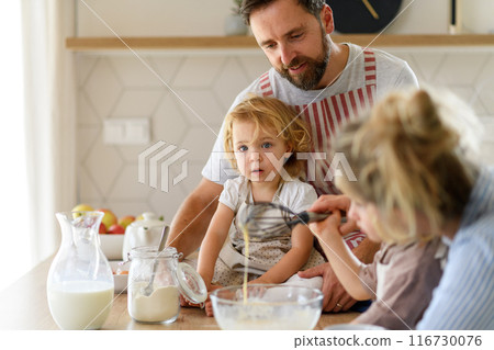 Young nuclear family making pancakes together. Parents and children in kitchen, preparing pancake batter, spending weekend day indoors. 116730076