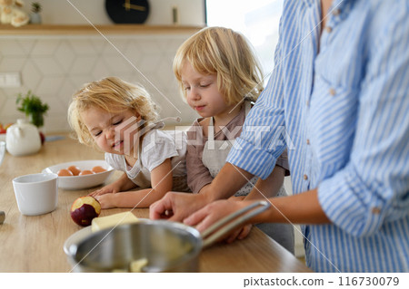 Mom and kids making pancakes together. Parent and children in kitchen, preparing pancake batter, spending weekend day indoors. 116730079