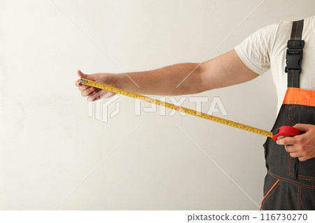 Hand holding tape measure profile. Construction worker measuring wall with tape measure, white background 116730270