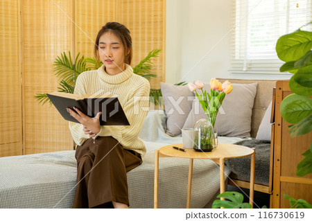 Young woman sitting and reading a book from the couch. 116730619