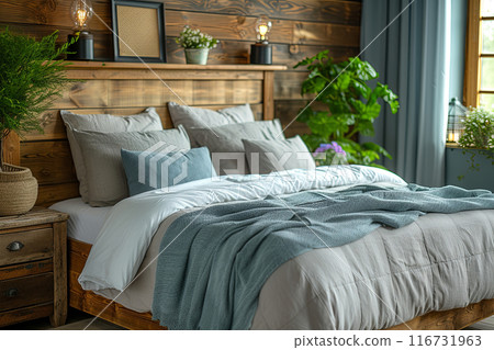 Bed with a blue blanket and pillows, and a potted plant on the night stand in a country house 116731963