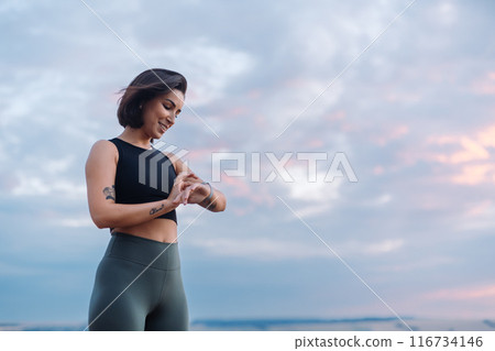A woman with a smartwatch is exercising outdoors in the morning, showing determination A woman with a smartwatch is exercising outdoors in the morning, showing determination 116734146