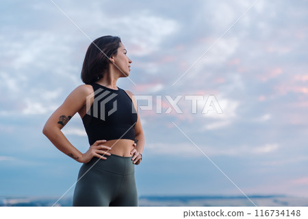 A woman in sportswear looks confidently during sunset, displaying strength and determination 116734148
