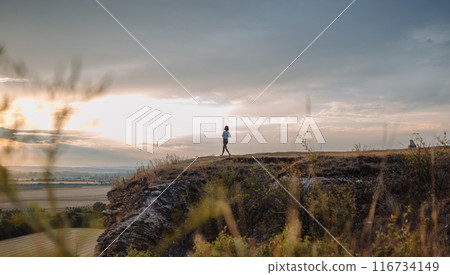 A man is running on a hill during sunset, offering a scenic view of the landscape and sky 116734149