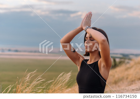 Woman Practicing Yoga Outdoors at Sunset in Serene Landscape with Focused Expression 116734150