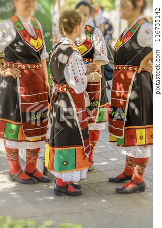 Group of women in traditional Bulgarian folk costumes with vibrant colors participating in a cultural festival outdoors Group of women in traditional Bulgarian folk costumes with vibrant colors participating in a cultural festival outdoors 116735142