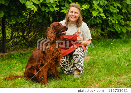 30s Woman in apron with dog tasting pink wine in vineyard. Portrait of pretty young woman holding glass of wine. Happy vintner drinks wine after successful grape harvesting. Harvest time, full body 30s Woman in apron with dog tasting pink wine in vineyard. Portrait of pretty young woman holding glass of wine. Happy vintner drinks wine after successful grape harvesting. Harvest time, full body 116735681