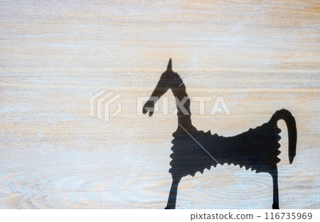 Shadow of a horse figurine on a textured flat wooden surface in bright sunny weather. 116735969