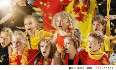 Group of children dressed in vibrant red, yellow, and black outfits spellbound watching their favorite team play on field, and golden confetti falling around them. Group of children dressed in vibrant red, yellow, and black outfits spellbound watching their favorite team play on field, and golden confetti falling around them. 116736334