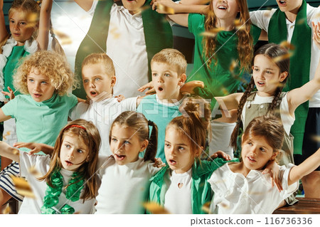 Children dressed in green and white cheering enthusiastically and hugs and golden confetti falling around them. Children dressed in green and white cheering enthusiastically and hugs and golden confetti falling around them. 116736336