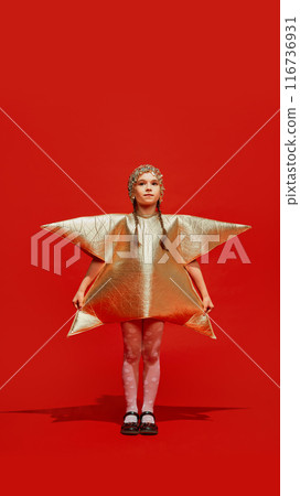 Portrait of beautiful young girl, child wearing festive costume in star shape, in golden color, posing against red studio background Portrait of beautiful young girl, child wearing festive costume in star shape, in golden color, posing against red studio background 116736931