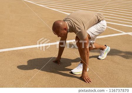 Sports trainer, starts, runner and handsome athletic man in running position on sports ground. Ready for run. Sunny hard shadow. Outdoors. Workout open air on urban background. Crossfit training 116737870