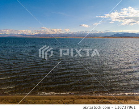Blue calm water in Issyk-Kul lake with mountains on background at autumn afternoon 116737961